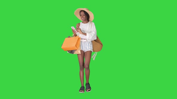 Happy African American Woman in Hat Walking and Using a Phone on a Green Screen, Chroma Key.