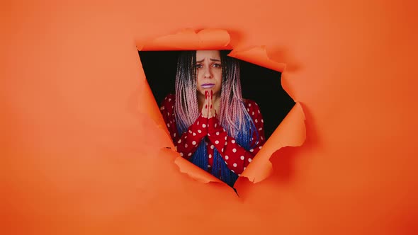 Young Woman Looking Out of Hole of Orange Background and Pleading
