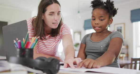 Happy caucasian woman and her african american daughter doing homework together