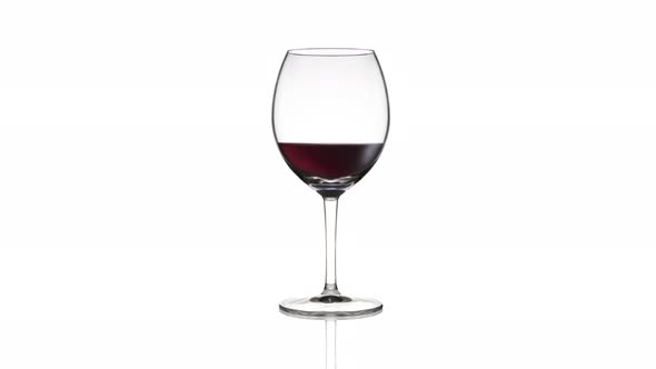 Empty Goblet Filling Up with Red Wine on White Background