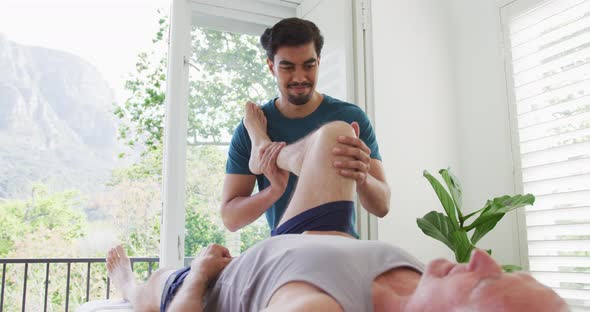 Biracial young male therapist treating leg of retired senior man at health club