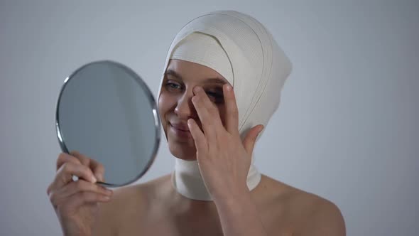 Woman in Headwrap Looking at Mirror Reflection, Satisfied With Plastic Surgery