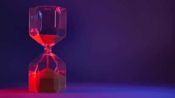 Glass Hourglass with Golden Sand on Purple Background