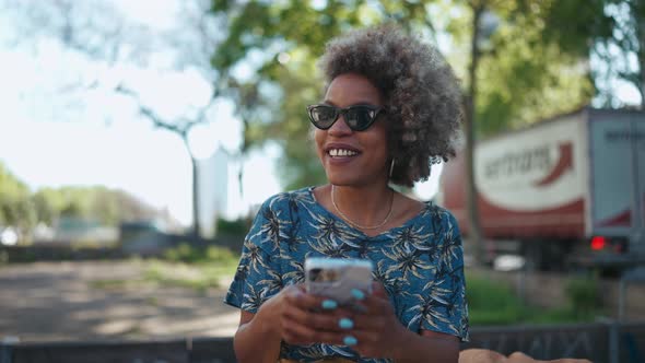 Positive African woman typing by phone and hugging her girlfriend