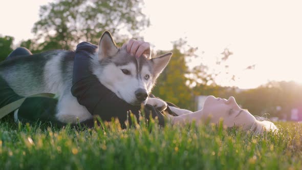Beautiful Young Woman Playing with Funny Husky Dog Outdoors in Park