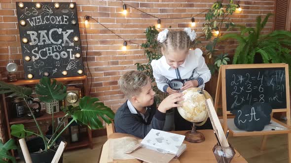 Schoolchildren - a boy and a girl are studying the globe with a magnifying glass