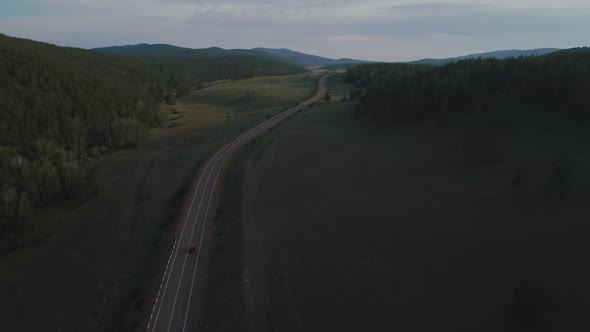 AERIAL, TOP DOWN: Dark Colored Car Driving Down an Asphalt Road Crossing the Vast Forest on a Sunny