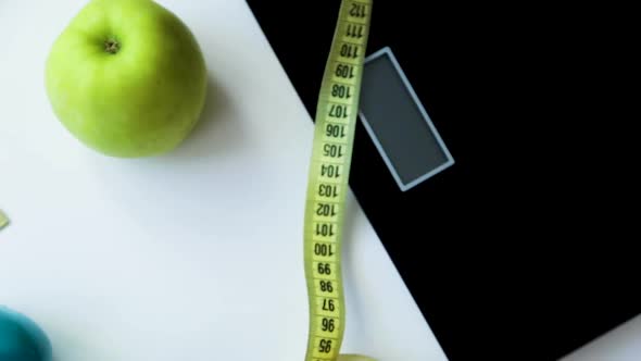 A Green Apple Scales a Fitness Elastic Band and Dumbbells are Wrapped Around a Measuring Tape