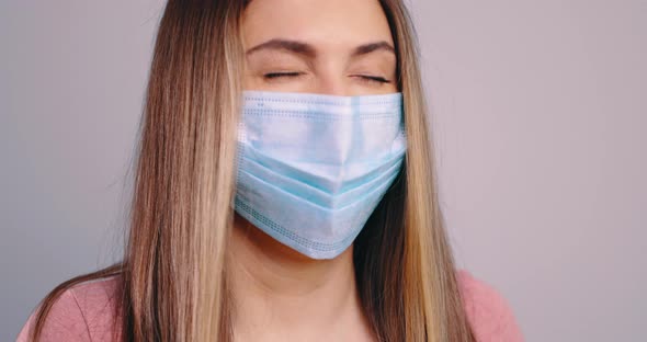 Close Up Portrait of Young Caucasian Woman Wearing Face Mask Sneezing Into Her Hands in Slow Motion