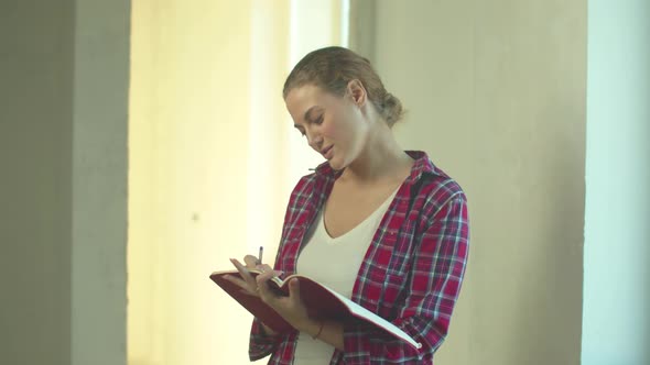 Woman Stands with a Notebook and Writes in It