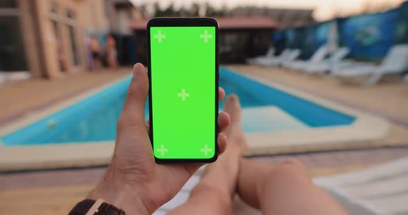 POV Male Hand Holding Smartphone with Green Screen Relaxing Near Pool