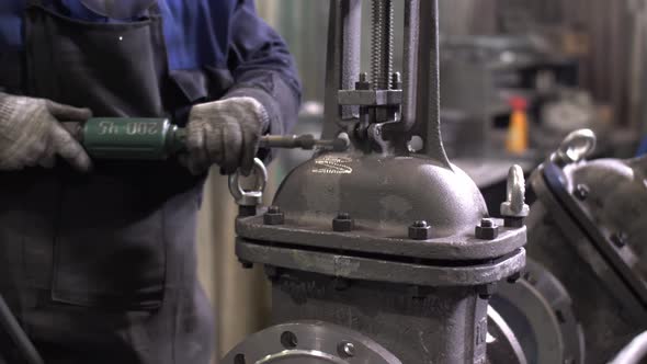 A Worker at the Plant Cleans the Manufactured Part with a Tool the Production Process at the Factory