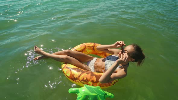 Happy Smiling Young Woman in Sunglasses Swimming on Inflatable Pineapple Floating Ring in Sea Water