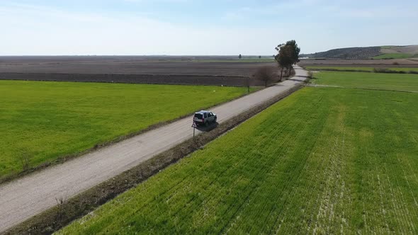 Car Drives on The Road Between Green and Brown Fields