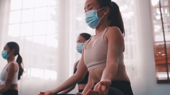 A group of Asian women wearing medical masks while doing yoga exercise at gym.