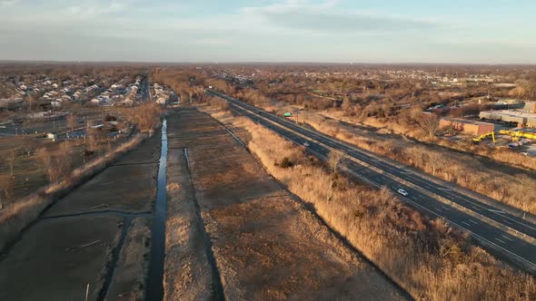 An aerial view over a dry, brown marsh on Long Island, NY. A long road runs next to it, shot on a su