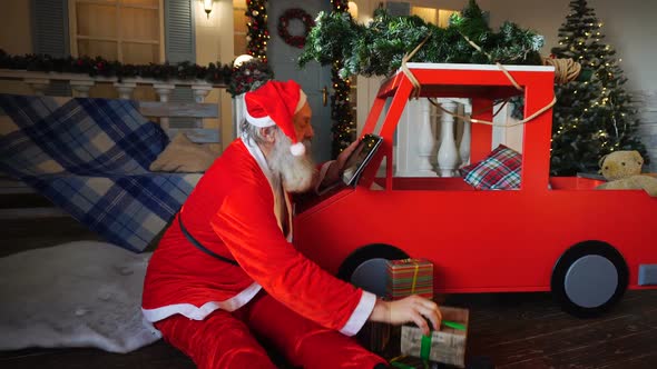 Funny Santa Claus Reading Children Desires on Tablet and Checking Gifts.