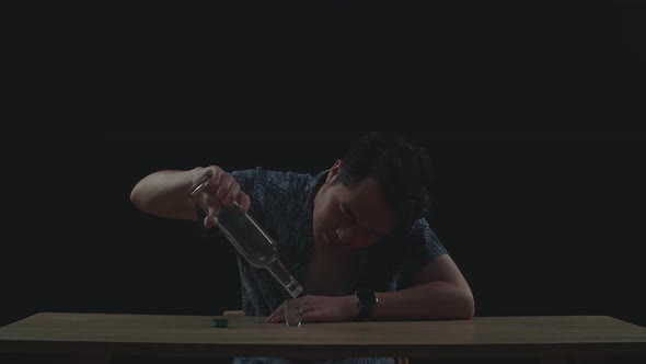 Drunk Asian Man Pours Vodka In A Shot Glass And Cheers Before Drinking In Black Background