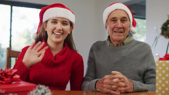 Happy caucasian senior father and adult daughter wearing santa hats making video call at home