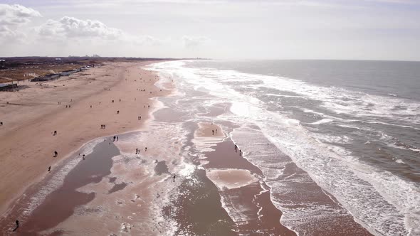 Aerial Flying Along Katwijk aan Zee Beach Coastline On Sunny Day With People Dotted Around. Slow Dol