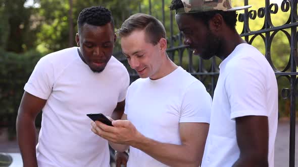 Three Multiracial Students Communicate with Each Other, Look at the Phone and Laugh