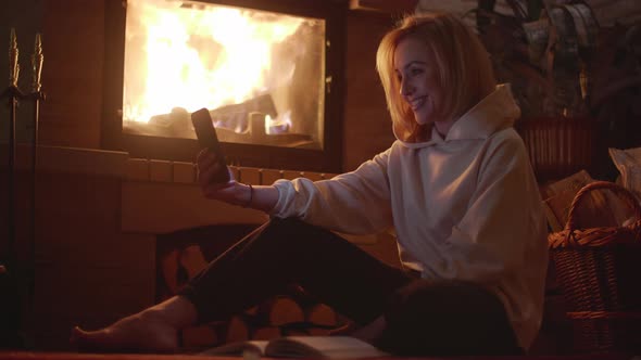 An European Young Woman Having Video Call Near Fireplace