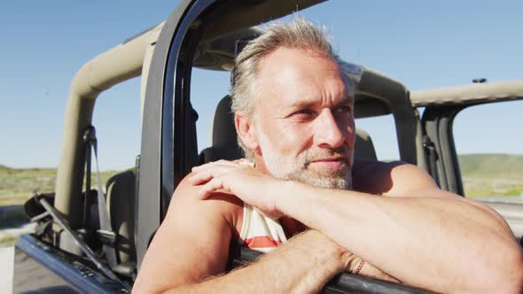 Happy caucasian man sitting in car enjoying the view on sunny day at the beach