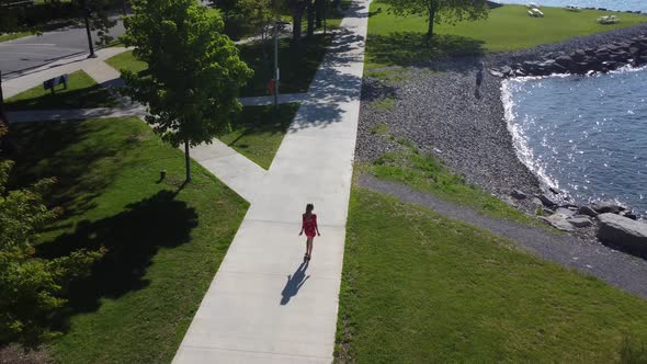 Aerial tilt down shot young women walking along a waterfront wearing a cute red dress