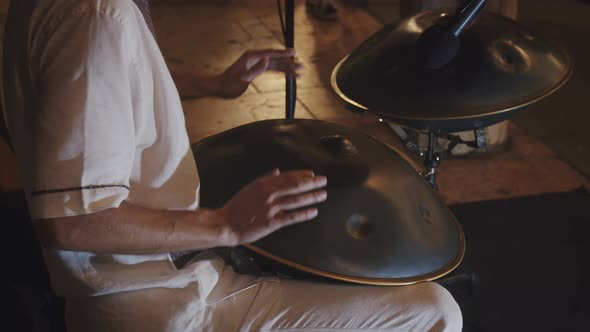 Busker artist in white robe plays handpan on the street during summer festival