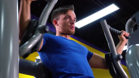 A Young Fit Man Trains on a Machine in a Gym - Closeup From Below