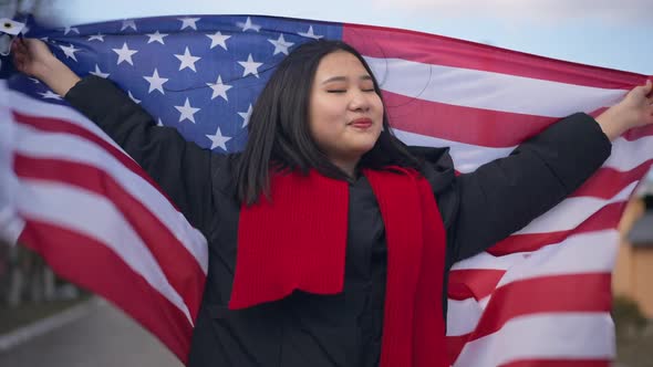 Happy Asian Young Woman Holding Fluttering American Flag in Hands and Wrapping in National Symbol