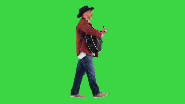 Man in a Cowboy Hat Singing and Playing the Guitar While Walking on a Green Screen Chroma Key