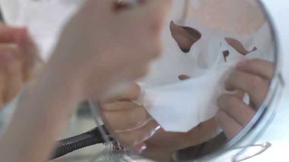Beautiful Girl Taking Off Moisturizing Tissue Mask in Front Mirror, Perfect Skin