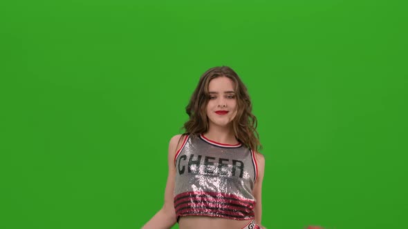 An Attractive Young Cheerleader in Uniform Performs a Jubilant Dance with Red Pompoms in the Studio