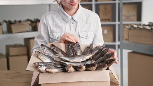 Small Business Charming Female Saleswoman Packing Dried Fish Into Boxes While Sitting on Background