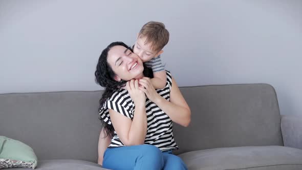 Happy Healthy Family Young Mom Hugs Cute Little Child Son Who Kisses Mother on Lips or Cheek Sitting