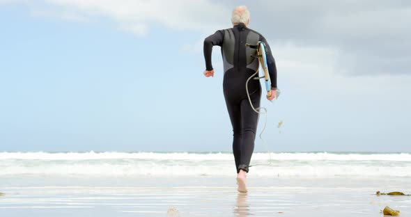 Rear view of old caucasian senior man running with surfboard at beach 4k