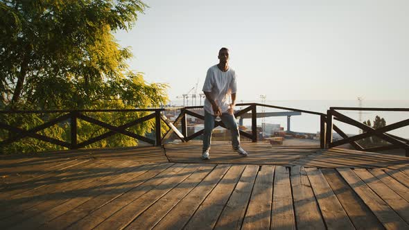 Young Male is Performing Windmill Movement While Breakdancing on Wooden Terrace Against Seascape of