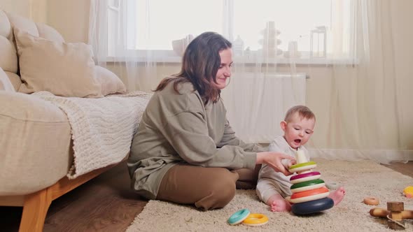 A happy child and mother play with a pyramid on the carpet in the home room, age 8 months