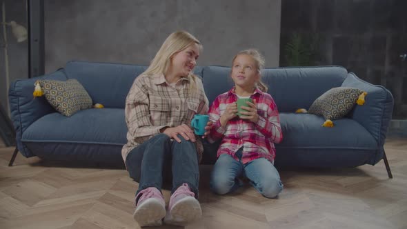 Positive Mom and Cute Daughter Drinking Tea Indoor