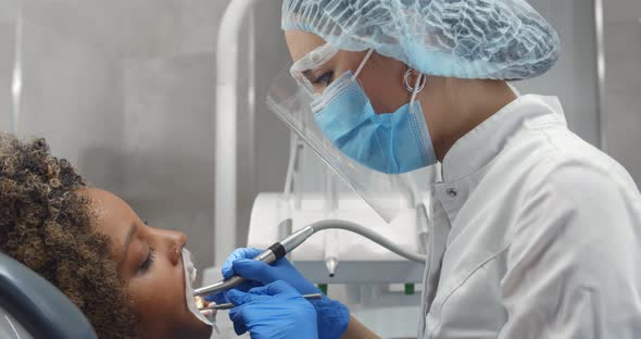 Female Dentist Treating Woman Patient with Opened Mouth