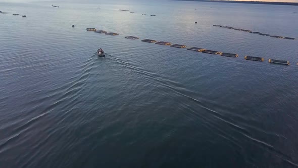 Drone following two fishermen in a small boat approaching fishing cages in the middle of a lake on a