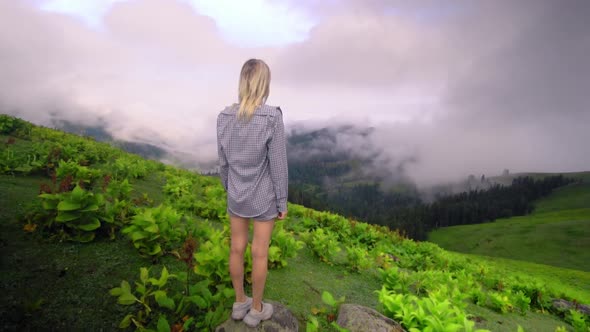 Young girl raised her hands up against background of clouds in mountains.