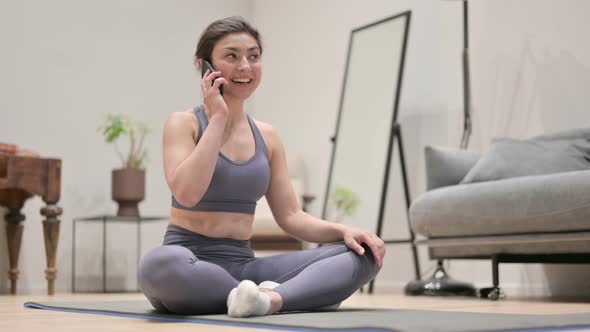 Young Indian Woman Talking on Smartphone on Yoga Mat at Home