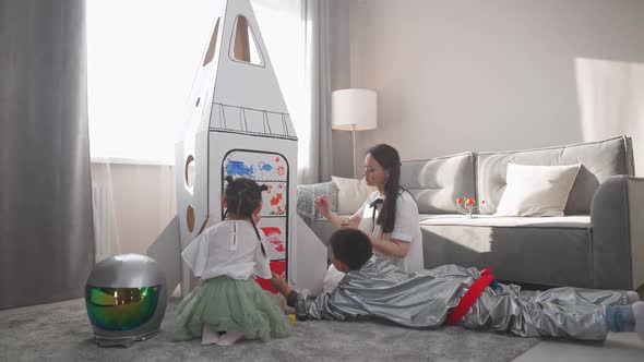 Asian Female with Kids Play in the Living Room at Home a Boy in an Astronaut Costume Lying on the