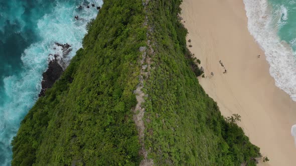 Aerial overhead shot of man walking down steep ridge on tropical coast