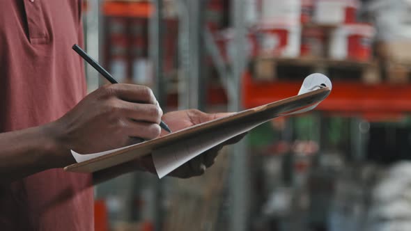 Close Up of Warehouse Worker Writing on Clipboard