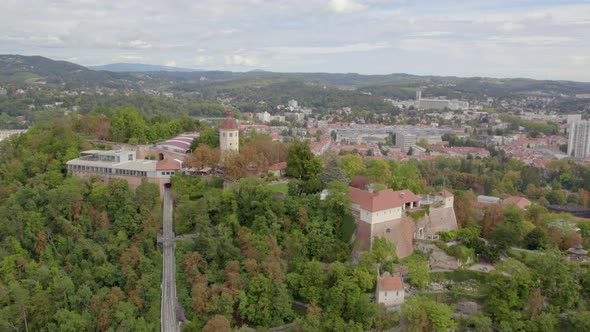 Aerial view wide orbit around historic hilltop Glokenturm tower on Graz's Schloßberg with views acro