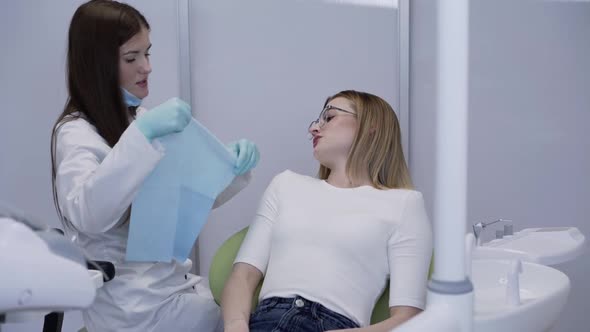 Female Dentist Preparing Patient for Treatment on Chair in Dental Clinic