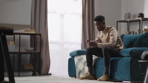 Afroamerican Man is Using Smartphone for Communication and Playing Games Sitting at Home Alone Black